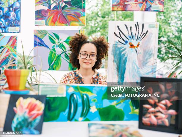 young latin woman artist selling her art at outdoor market - art show stock pictures, royalty-free photos & images