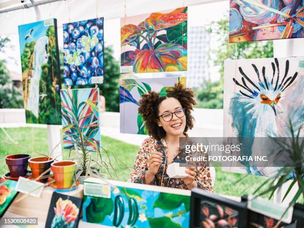 young latin woman artist selling her art at outdoor market - art show stock pictures, royalty-free photos & images