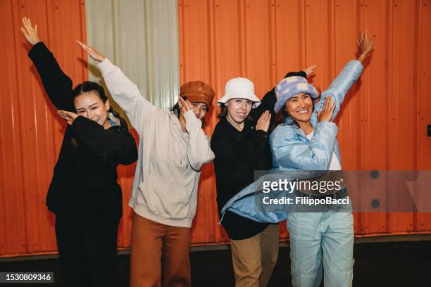 portrait of four friends wearing cool street style clothes making dabbing movement against an orange wall - dab dance stock pictures, royalty-free photos & images