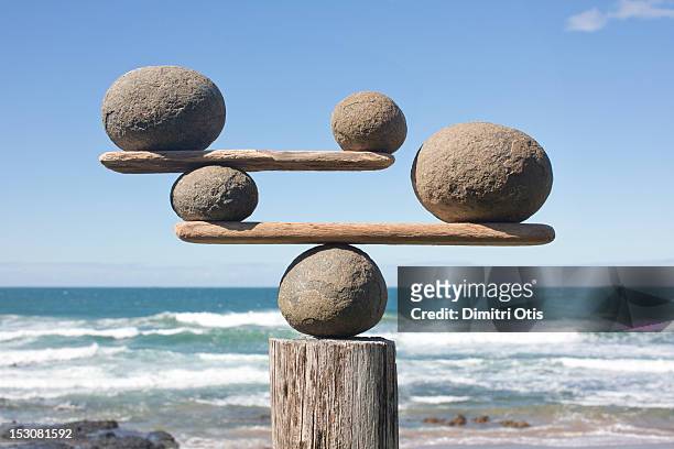 rocks balancing on driftwood, sea in background - equilibrio fotografías e imágenes de stock