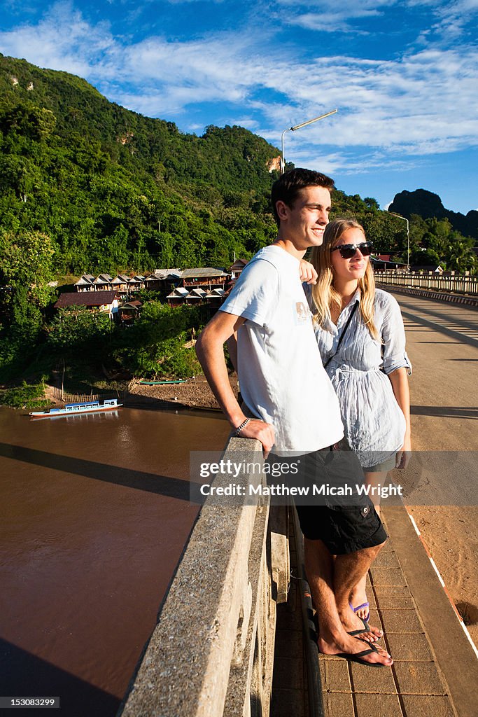 A couple watches the sunset from a bridge.