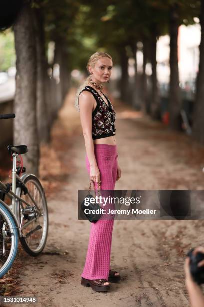 Olga Karput seen outside Chanel show wearing red and gold Chanel earrings and necklace, Chanel knitted vest, pink wide leg pants, black Chanel...