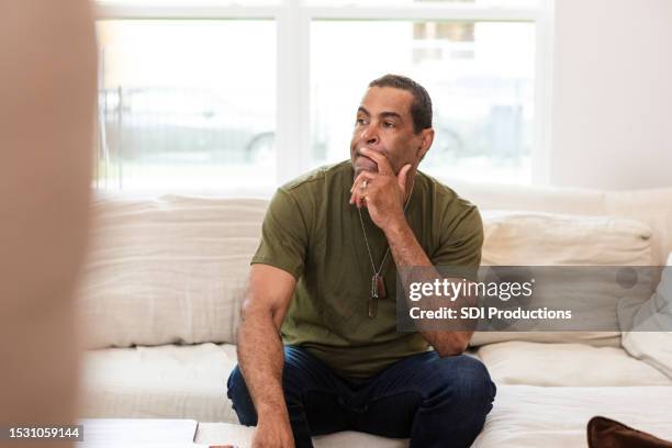 sitting on sofa, retired mature male soldier deals with memories - veteran memorial stock pictures, royalty-free photos & images