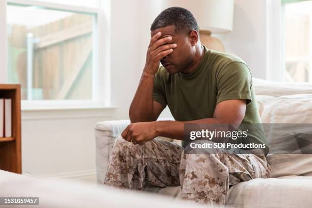distraught male soldier sits alone in living room - oorlogsneurose stockfoto's en -beelden