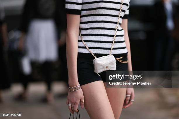 Guest seen outside Chanel show wearing Chanel top in black with white stripes, small white Chanel Crossbody bag, gold Cartier bracelets and black...