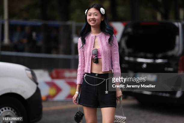Guest seen outside Chanel show wearing Chanel flowers in hair, pink Chanel cardigan, pink bra top, black Chanel shorts with a silver Chanel logo...
