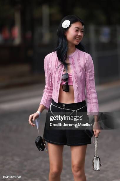 Guest seen outside Chanel show wearing Chanel flowers in hair, pink Chanel cardigan, pink bra top, black Chanel shorts with a silver Chanel logo...