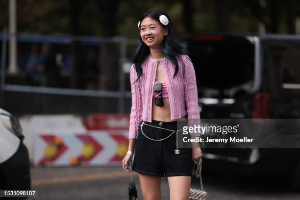 Guest seen outside Chanel show wearing Chanel flowers in hair, pink Chanel cardigan, pink bra top, black Chanel shorts with a silver Chanel logo...