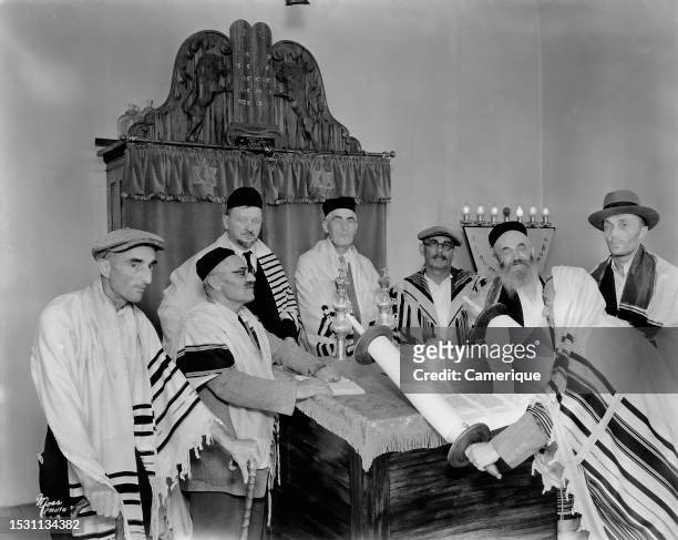 Group of eight men in robes sitting at the altar looking at script during Hebrew synagogue services