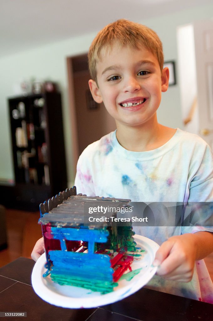 Boy holding house made of craft sticks