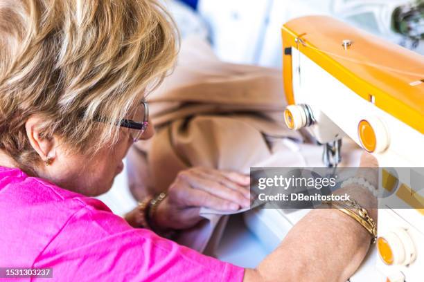 retired lady tailor sewing in natural light with a sewing machine, occupying her spare time. sewing, hobby, dressmaker and tailor concept. - vintage syringe stock pictures, royalty-free photos & images