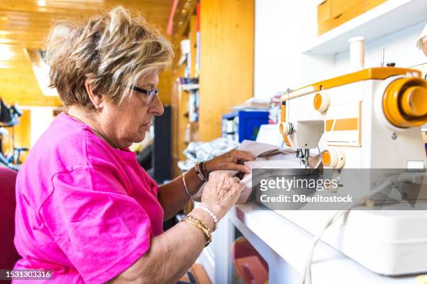 retired lady tailor sewing in natural light with a sewing machine, occupying her spare time. sewing, hobby, dressmaker and tailor concept. - vintage syringe stock pictures, royalty-free photos & images