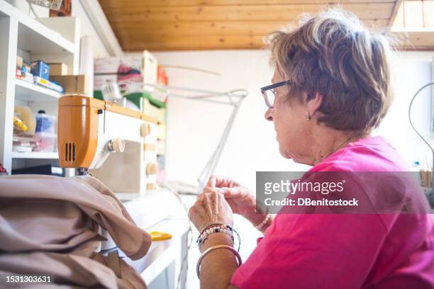 retired lady tailor sewing in natural light with a sewing machine, occupying her spare time. sewing, hobby, dressmaker and tailor concept. - vintage syringe stock pictures, royalty-free photos & images