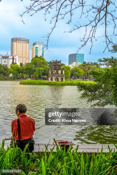 des gens sur la rive du lac hoan kiem avec la célèbre pagode de la tortue et des bâtiments modernes en arrière-plan à hanoi, au vietnam. concept de voyage et de paysage. - hoan kiem lake photos et images de collection