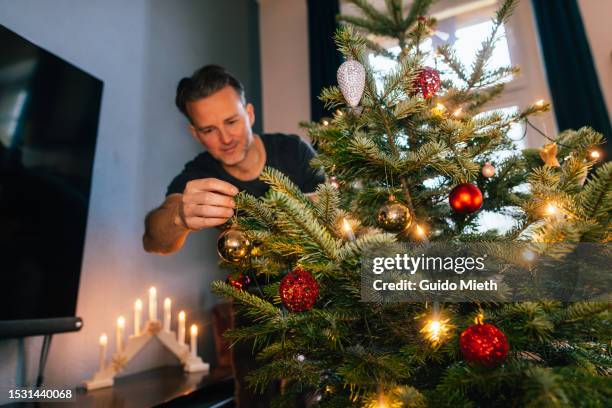 man decorating christmas tree at home. - decorating-the-christmas-tree stock pictures, royalty-free photos & images