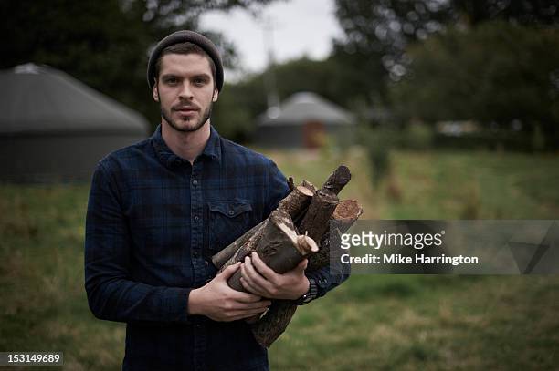 man holding firewood on glampsite. - young men camping stock pictures, royalty-free photos & images