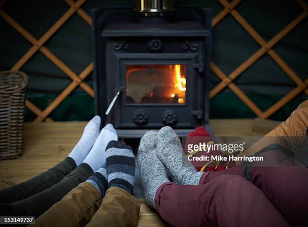 friends sitting with feet around log fire in yurt. - yurt stock pictures, royalty-free photos & images