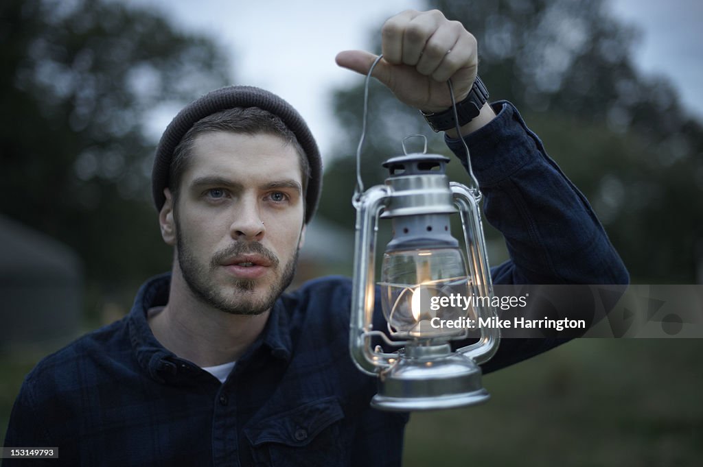 Man walking around glampsite holding lantern.