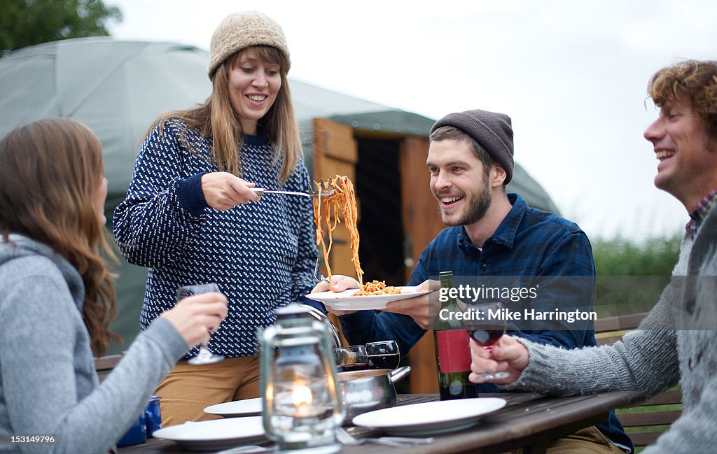 Young woman serving pasta to fellow glampers.