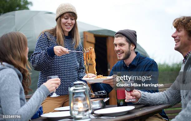 young woman serving pasta to fellow glampers. - camping friends stock pictures, royalty-free photos & images