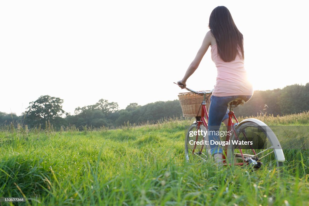 Woman riding bike through country meadow.