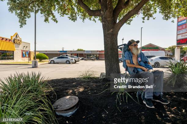 Randy Twede sits in the shade while waiting for the bus on July 10, 2023 in Austin, Texas. Twede is a homeless resident living in Austin, Texas....