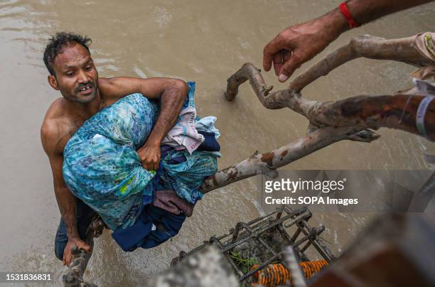 Man struggles to climb to a bridge with his belongings after being displaced by rising water levels in the Yamuna River following heavy monsoon rains...