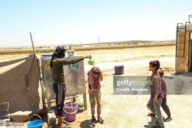 Man cools a boy with water next to children as civilians struggle with protecting themselves from the dangers of extreme heat at the refugee camp, in...