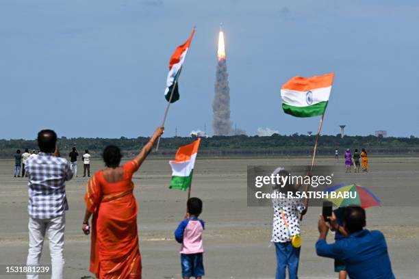 People wave Indian flags as an Indian Space Research Organisation rocket carrying the Chandrayaan-3 spacecraft lifts off from the Satish Dhawan Space...