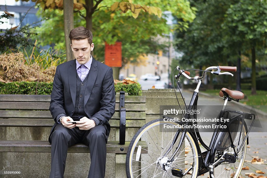 Businessman with bicycle in park texting on mobile