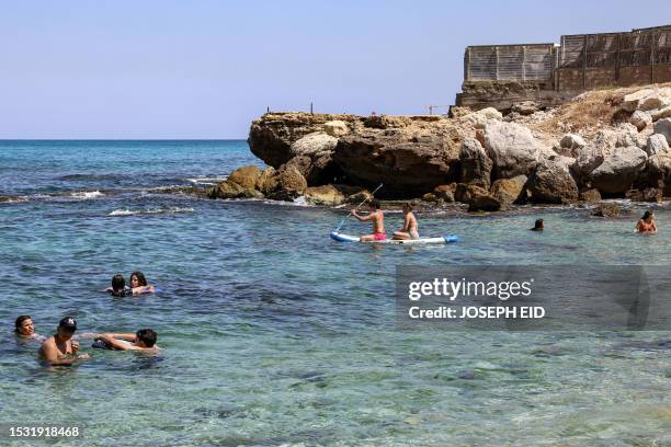 Boy and a girl ride a paddle board past other swimmers by a beach off Lebanon's northern coastal village of Kfarabida on July 12, 2023.