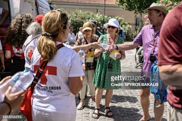 Volunteers of the Hellenic Red Cross hand out bottles of water at the bottom of the Acropolis hill in Athens, on July 14, 2023. The ministry of...