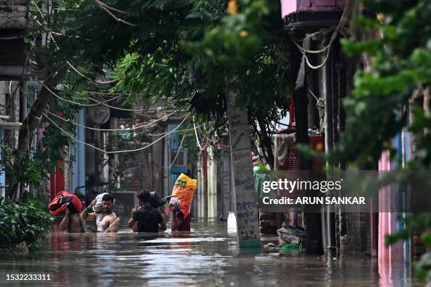 Flood-affected people carrying their belongings wade through flood water after river Yamuna overflowed following heavy monsoon rains in New Delhi on...