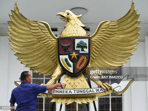An Indonesian man cleans the country's symbol Garuda Pancasila, a mythical golden eagle with a heraldic shield on its chest, which is attached on a...