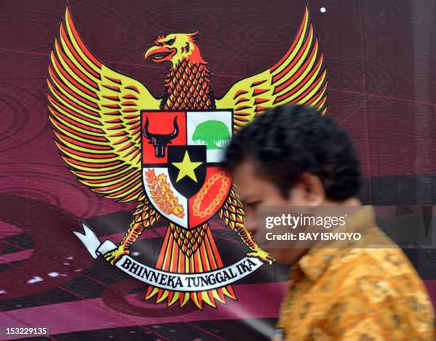 Pedestrian walks past the Indonesian symbol of Garuda Pancasila , a mythical golden eagle with a heraldic shield on its chest, which is attached on a...