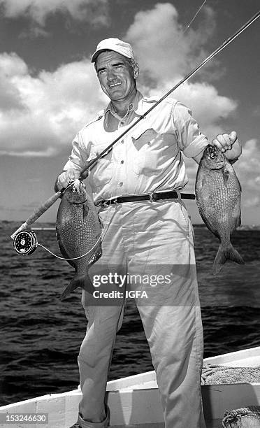 Joe Brooks stands in a small boat holding two Bermuda chubs caught on fly circa 1950.