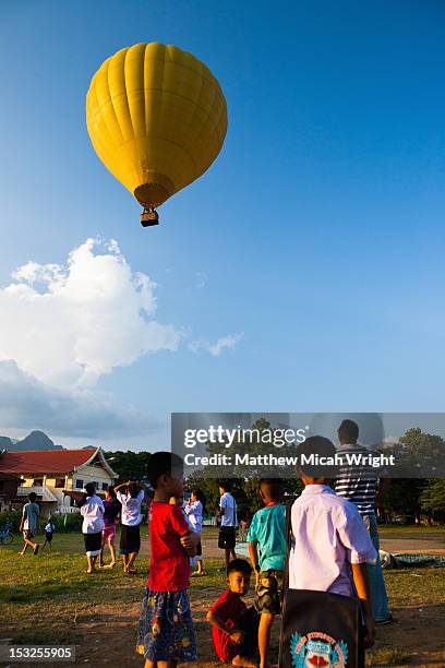 a hot air balloon ascends over a local village. - vang vieng balloon stock pictures, royalty-free photos & images