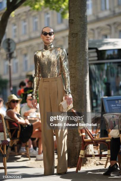 Guest wears black butterfly sunglasses, a gold embroidered sequined turtleneck / long sleeves body, high waist beige suit pants, a beige matte...