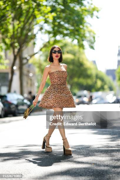 Heart Evangelista wears black cat eyes sunglasses from Saint Laurent, a beige brown with embroidered brown / green / silver sequined shoulder-off /...