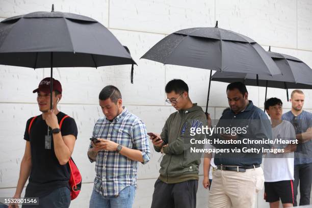 Apple customers wait in the line with umbrellas and ready to purchase the new products at the Highland Village Apple store before the doors open at 8...
