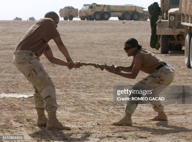 Army Private First Classes Deonte Sanders helps Quinetta Pryor twist away laundry waters on her uniform at a US military desert camp of the 3rd...
