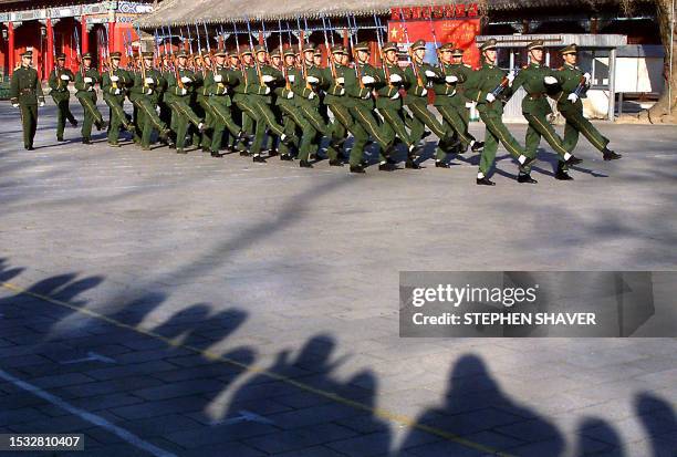 Curious onlookers and their shadows watch People's Liberation Army soldiers perfect their goose-stepping march during drills outside their barracks...
