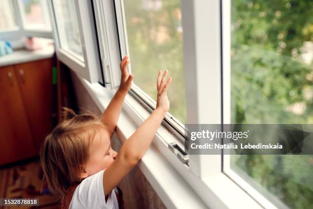 window safety precaution: toddler curiously reaching for windowsill, highlighting window fall risk - moustiquaire photos et images de collection