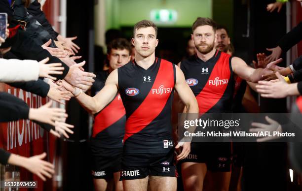 Zach Merrett of the Bombers runs onto the field for his 200th match during the 2023 AFL Round 18 match between the Geelong Cats and the Essendon...
