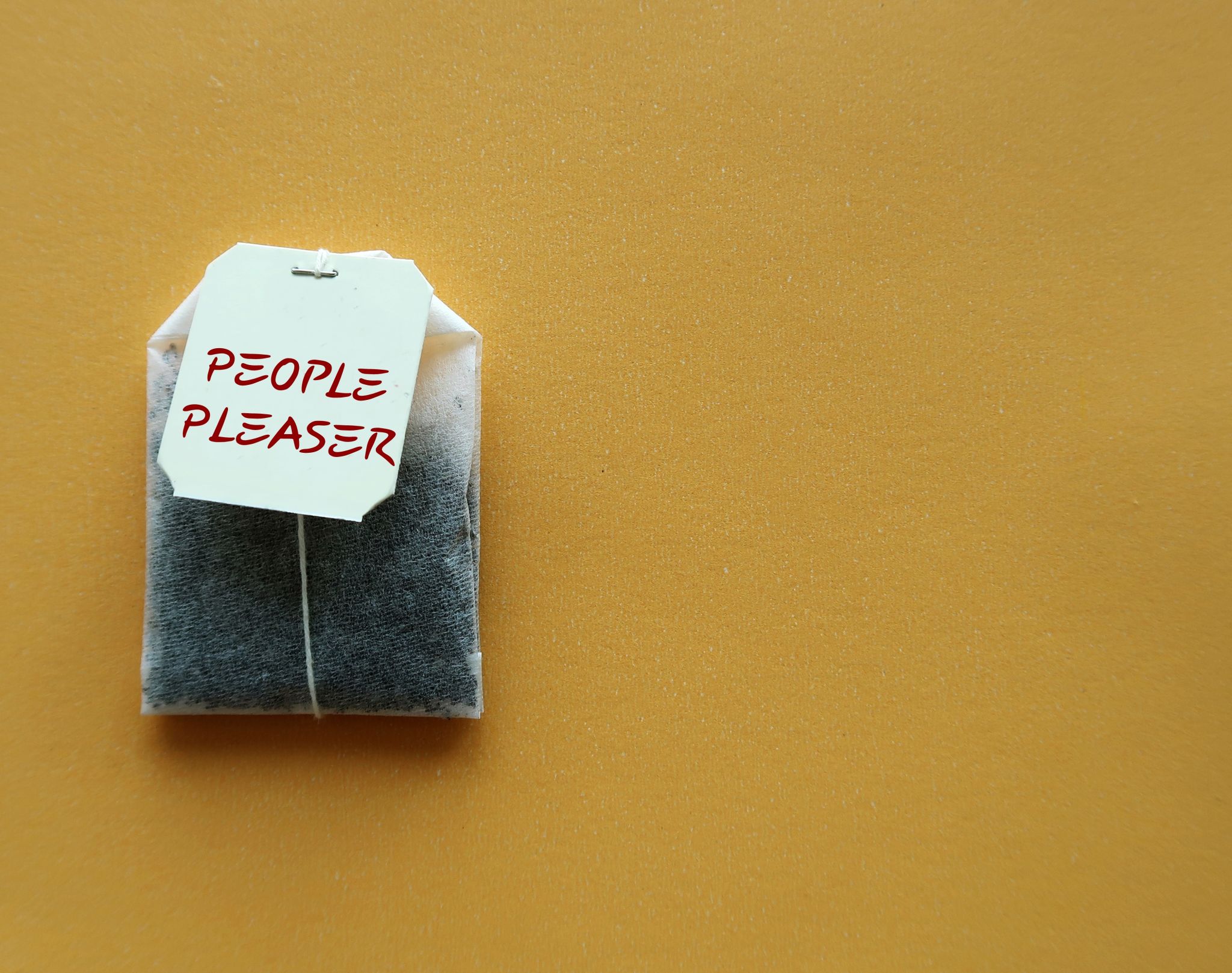 Teabag on yellow copy space background with text PEOPLE PLEASER, concept of one who tries hard to make others happy even go out of their way, time or resources,overly concerned with pleasing others Teabag on yellow copy space background with text PEOPLE PLEASER, concept of one who tries hard to make others happy even go out of their way, time or resources,overly concerned with pleasing others