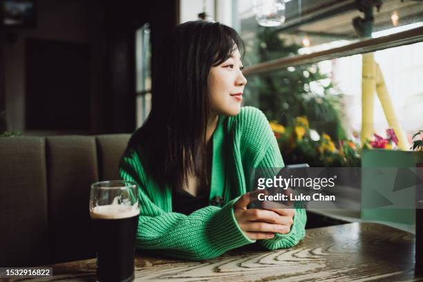 asian beautiful woman holding her smartphone and looking outside in a restaurant - poes stock pictures, royalty-free photos & images