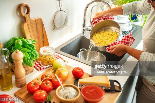 mujer drenando el agua de los espaguetis usando un colador - colador fotografías e imágenes de stock