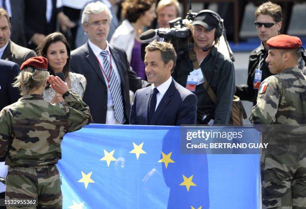 French President Nicolas Sarkozy smiles next to national TV host Marie Drucker at the end of the troops parade for Bastille Day celebrations on the...