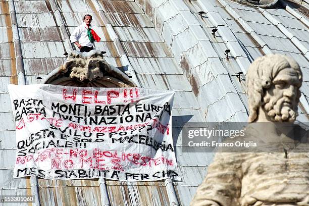 Marcello Di Finizio stands above a window ledge next to a banner displaying messages of protest against the Monti government and the Europe Union on...