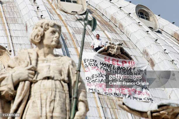 Marcello Di Finizio stands above a window ledge next to a banner displaying messages of protest against the Monti government and the Europe Union on...